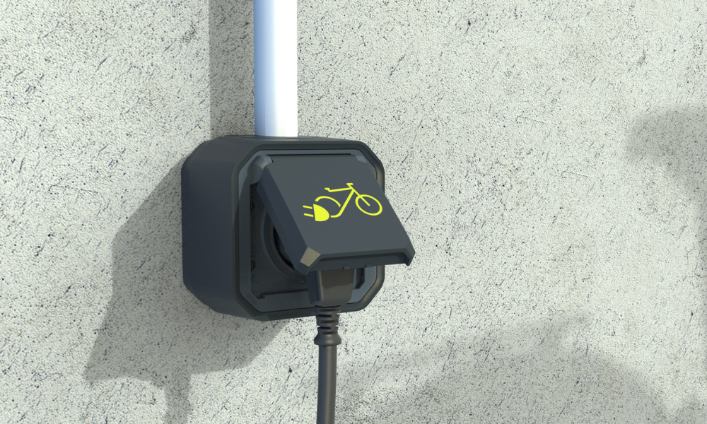 Gniazdo do ładowania rowerów elektrycznych i innych pojazdów elektrycznych. Z rowerem podłączonym do ładowania. Na gnieździe znajduje się żółty piktogram roweru