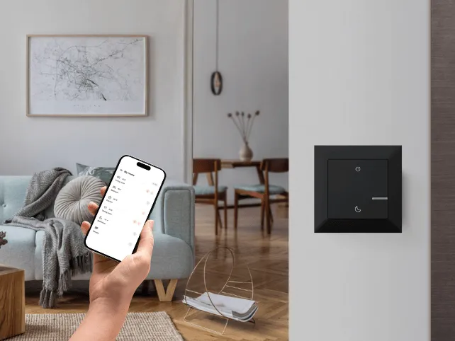 Sterowanie oświetleniem z aplikacji w telefonie obok czarnego panelu Legrand na ścianie