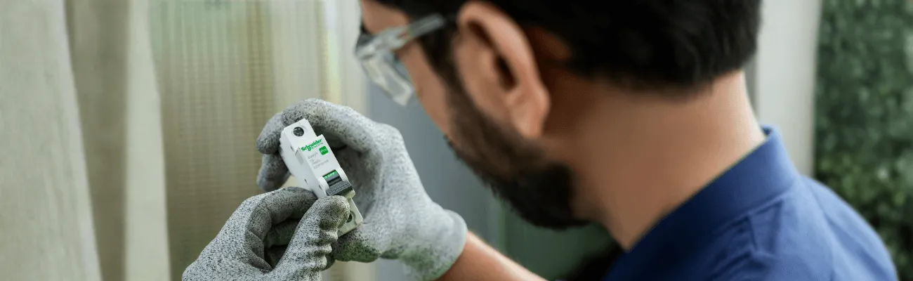 Elektryk w rękawicach i okularach ochronnych trzyma wyłącznik nadprądowy Schneider Easy9 Pro