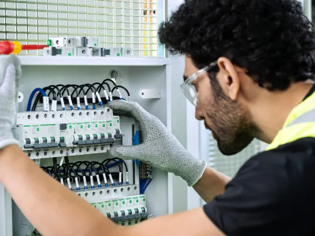 Elektryk w okularach ochronnych podłącza przewody do rozdzielnicy Schneider
