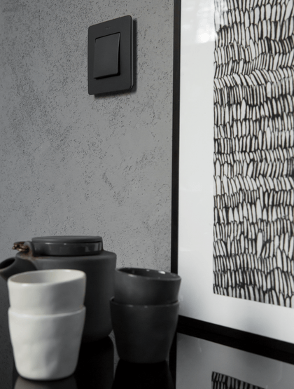 Czarny włącznik na szarej betonowej ścianie obok grafiki i ceramicznych kubków